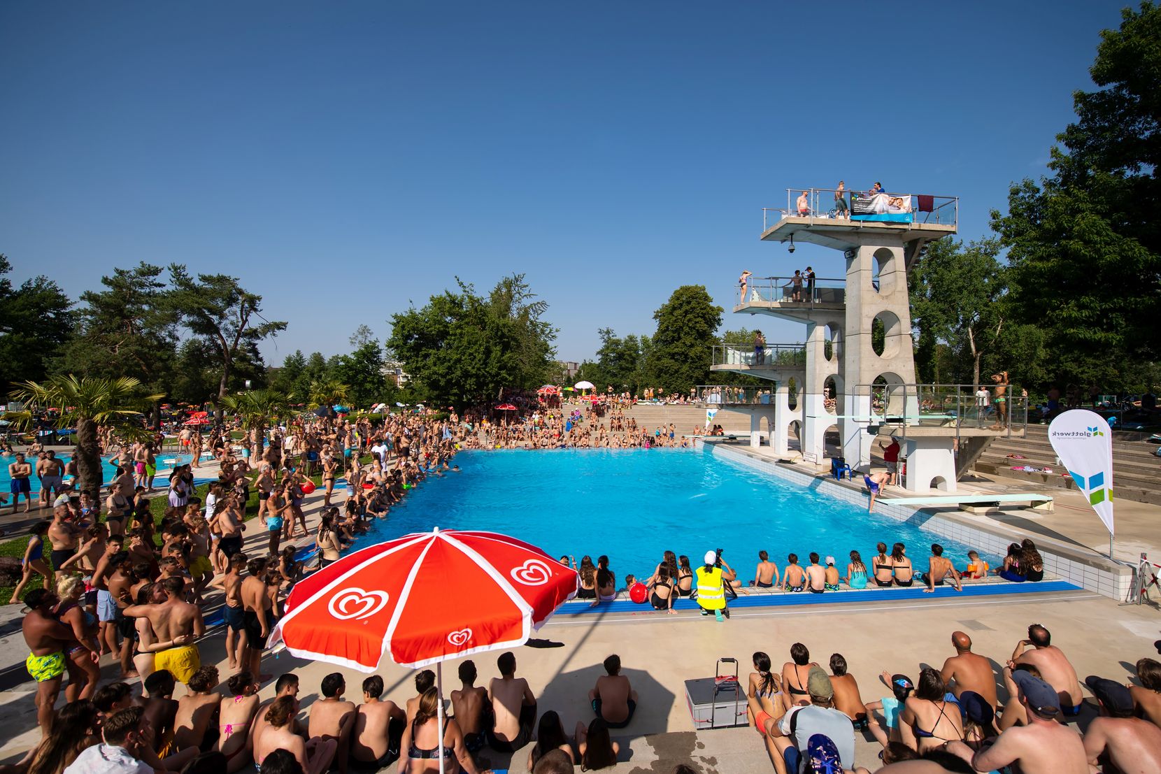 Ein Sprungturm im Freibad mit vielen Zuschauern.